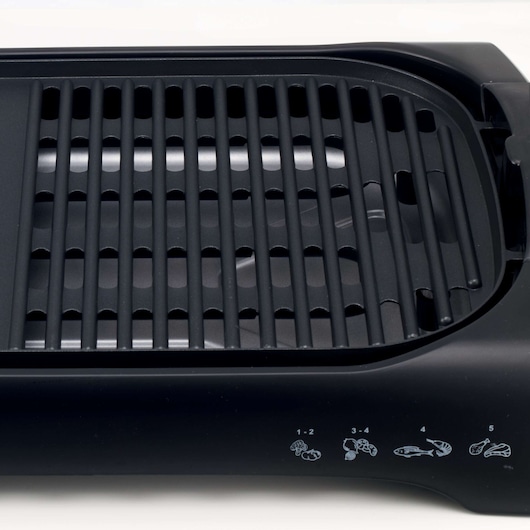 Close-up view of a BLACK+DECKER electric grill, showing the black grill plate and settings panel with illustrated temperature icons for different types of food.