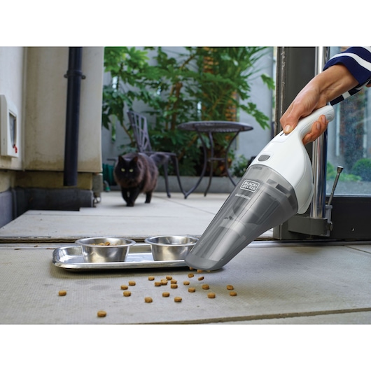 BLACK+DECKER NVB215WN handheld vacuum cleaning pet food near bowls on floor, outdoor scene with cat in background.