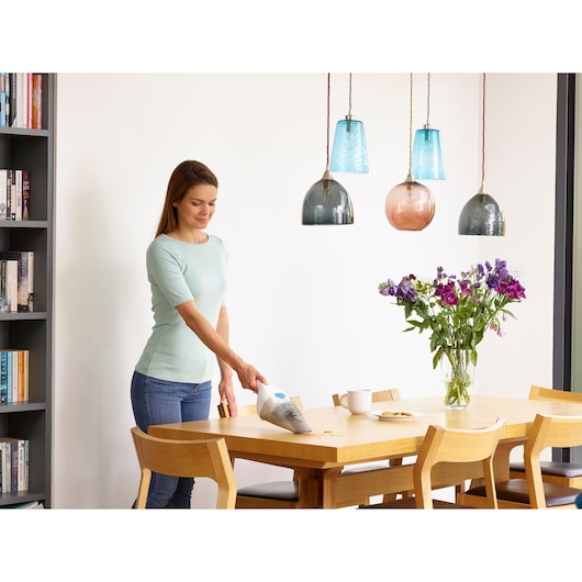 BLACKDECKER NVC115JL handheld vacuum cleaning crumbs on dining table near vase of flowers.