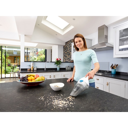 BLACK+DECKER NVC115JL handheld vacuum cleaning oats on a kitchen counter near a bowl and fruit plate.