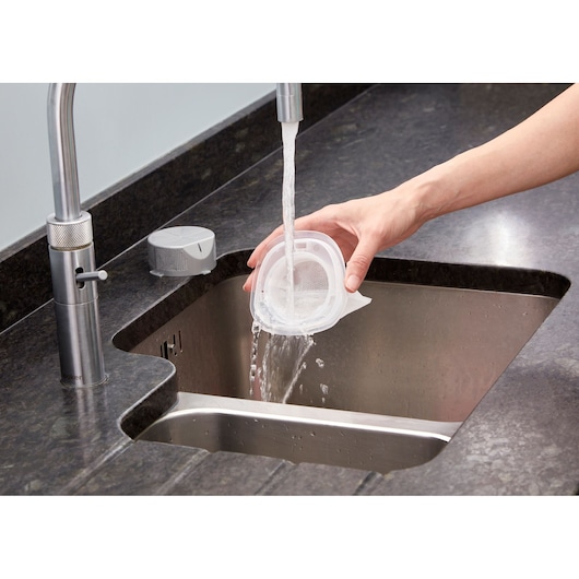 BLACK+DECKER NVC115WA vacuum filter being rinsed under faucet in kitchen sink.