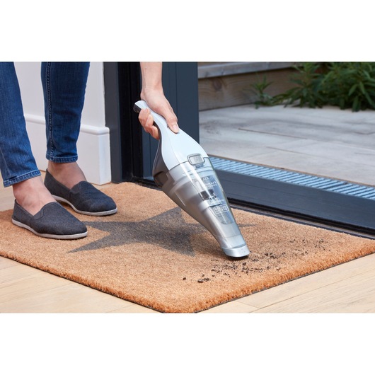 BLACKDECKER NVC215W handheld vacuum cleaning dirt from a brown doormat near a doorway.