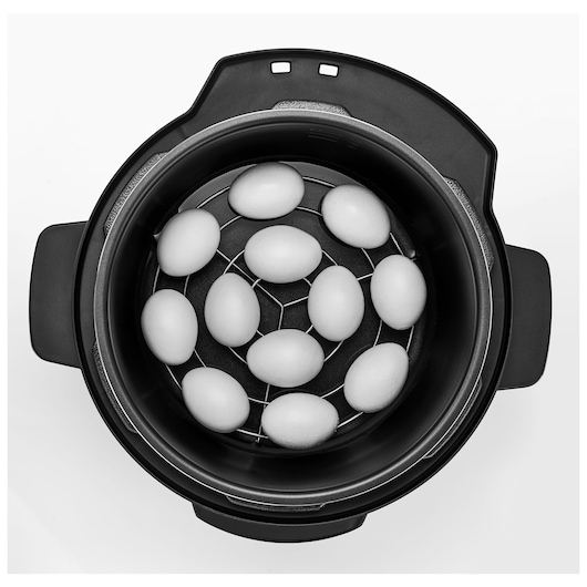 BLACKDECKER PCP1010 pressure cooker top view with eggs on metal rack, black housing, white background.