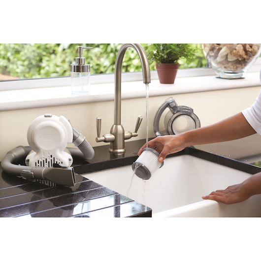 BLACKDECKER PD1420LP handheld vacuum next to a kitchen sink, filter being rinsed under running water.