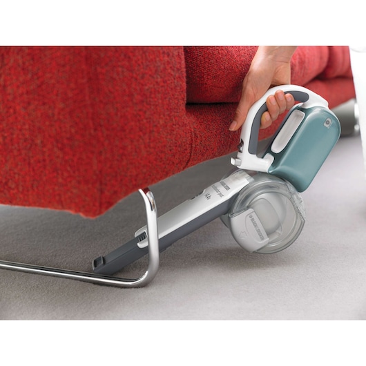 BLACK+DECKER PV1425N handheld vacuum cleaner being used under a red sofa for tight space cleaning.