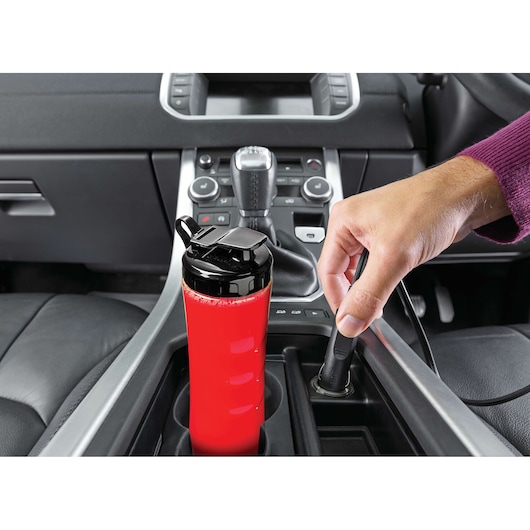 BLACKDECKER SBX300BCG portable blender cup with red smoothie in a car cup holder, hand plugging it in.