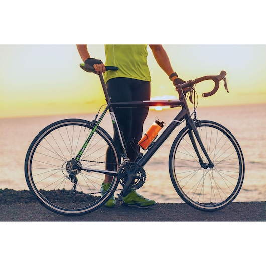 BLACKDECKER SBX300BCG bottle flask on a road bike frame held by a cyclist at sunset by the sea.