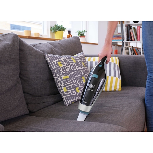 BLACK+DECKER SVA420B handheld vacuum cleaner used on a grey sofa in a living room setting.