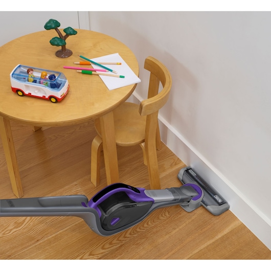BLACKDECKER SVJ520BFSP cordless stick vacuum cleaning under children's wooden table and chair on hardwood floor.
