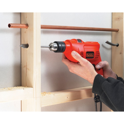 BLACKDECKER TM500 corded drill in use drilling through wood near copper pipes, close-up view.