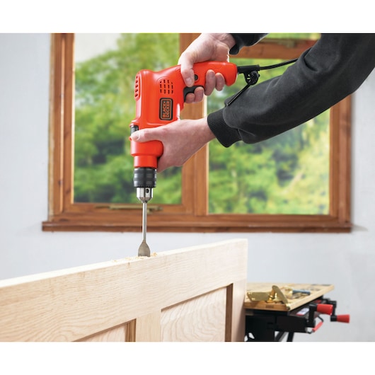 BLACKDECKER TM500 electric drill being used to drill wood indoors, side angle.