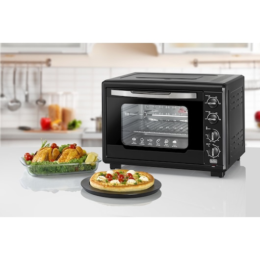 BLACKDECKER TRO55RDG countertop oven with control knobs, glass door, shown with roasted chicken and pizza in a kitchen.