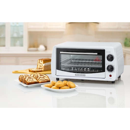 BLACK+DECKER TRO9DG compact toaster oven with two control knobs, pictured on a kitchen counter with baked goods.