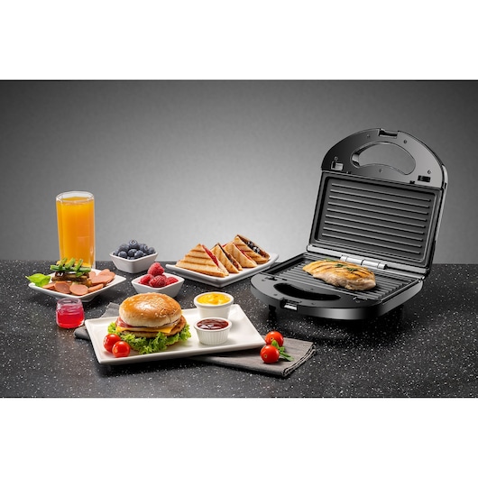 BLACKDECKER TS2120 sandwich maker with grilled chicken, burger, sauces, juice and assorted breakfast foods on black surface.