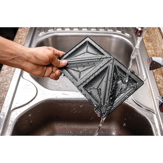 BLACKDECKER TS2120 sandwich maker plate being washed under running water in a kitchen sink.