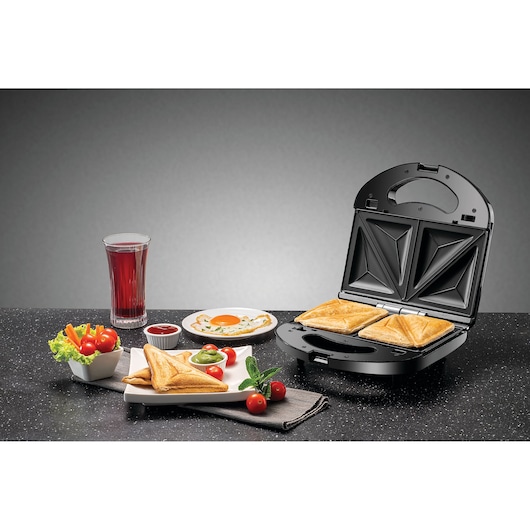 BLACKDECKER TS2130 sandwich maker with toasted sandwiches, juice, salad, and breakfast on a kitchen counter.