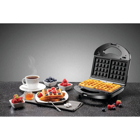 BLACKDECKER TS2130 waffle maker with two square waffles, breakfast setup with cup of coffee, berries, and honey.
