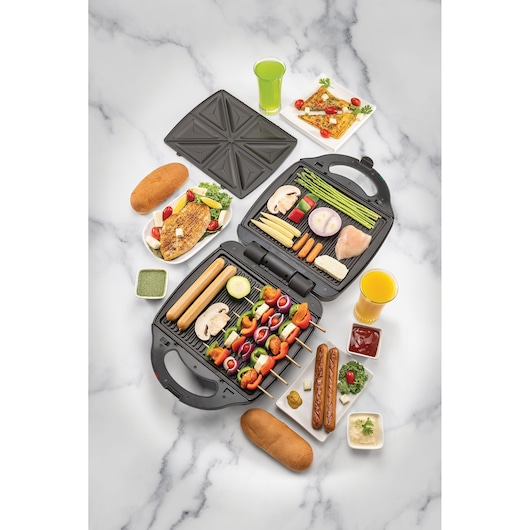 BLACKDECKER TS4120 grill and sandwich maker, top view on white background, shown with assorted grilled vegetables, sausages, bread, and drinks.