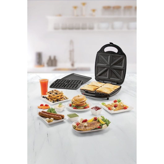 BLACKDECKER TS4130 sandwich maker with open lid, four sandwiches inside, waffle plates, and assorted food dishes on a kitchen counter.