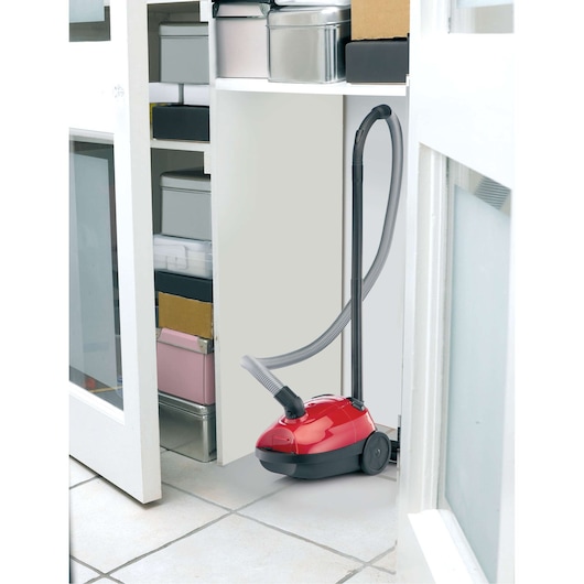 BLACK+DECKER VM1200 red canister vacuum cleaner with hose stored in a white cabinet.