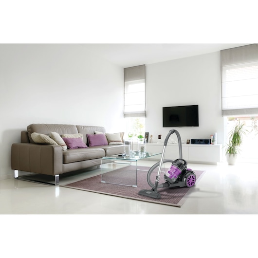 BLACKDECKER VM1880 canister vacuum cleaner with purple accents on a rug in a modern living room, front angle.