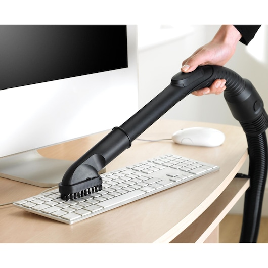 BLACKDECKER VM2825 vacuum cleaner brush attachment cleaning keyboard on desk, side angle.