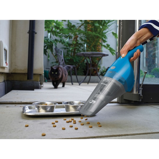BLACK+DECKER WDB215WA handheld vacuum cleaning spilled pet food near metal bowls, outdoor patio, side view.