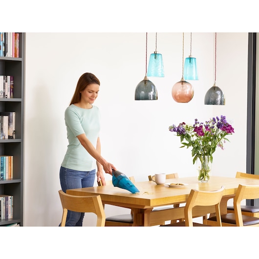 BLACKDECKER WDC215WA handheld vacuum cleaning crumbs from wooden dining table in modern home setting.