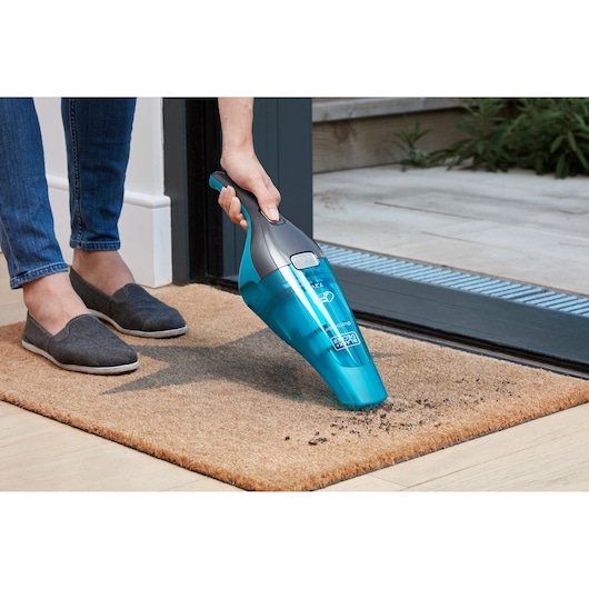 BLACKDECKER WDC215WA handheld vacuum cleaning debris on beige doormat near door.