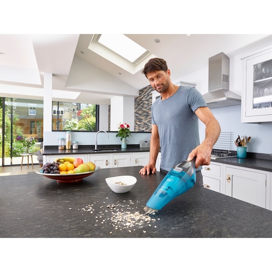 BLACKDECKER WDC215WA handheld vacuum cleaning oats on kitchen counter, fruits and bowl nearby.