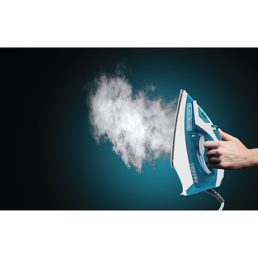 Photo of BLACK+DECKER X1575 steam iron emitting steam, shown from side angle, hand adjusting temperature dial.
