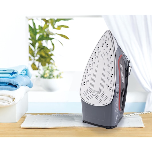Photo of BLACKDECKER X2050 steam iron standing upright on table, visible soleplate, folded towels in background.