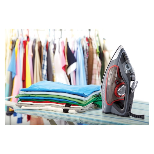 BLACKDECKER X2050 steam iron with black and red design on ironing board next to folded clothes, X2050_E2.