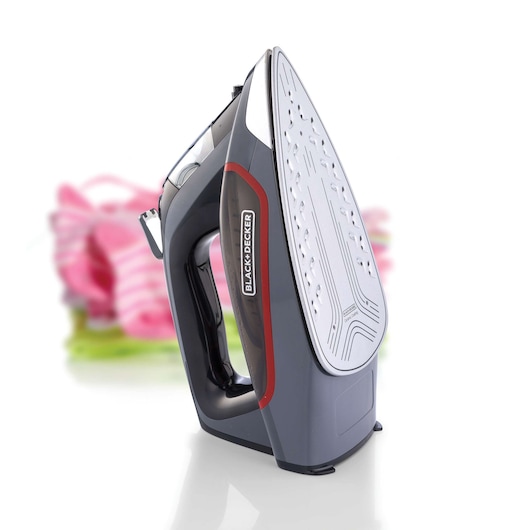 BLACK+DECKER X2050 steam iron, gray and black with red trim, upright on white background, pink folded clothes behind.