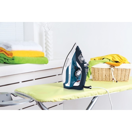 BLACKDECKER X2150 steam iron on green ironing board, basket and folded towels in background.