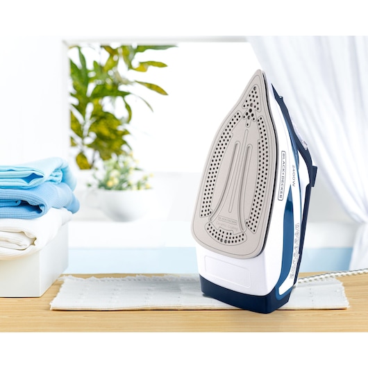 Photo of BLACKDECKER X2150 steam iron upright on table, visible ceramic soleplate, stack of folded towels nearby.