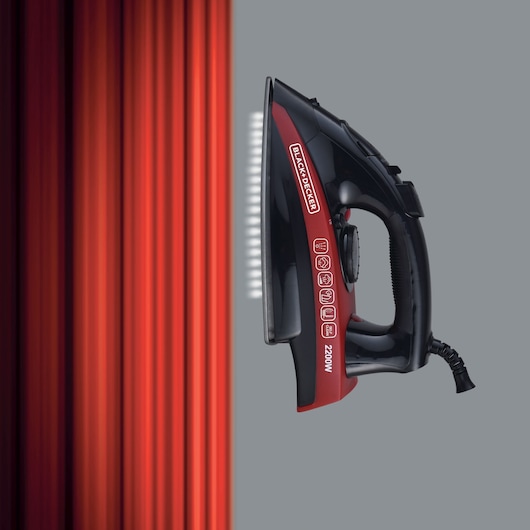 Photo of BLACK+DECKER X2200 steam iron, black and red, side view, with steam effect, next to red vertical lines.